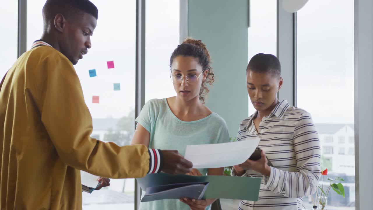 Diverse male and female creative colleagues in discussion, looking at documents and tablet