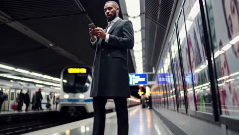 man using phone on a subway platform while waiting for a train