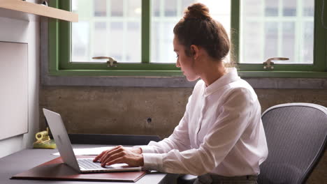 mujer joven trabajando en una computadora portátil sola en una oficina, de cerca