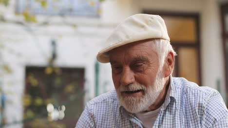 Primer-Plano-Del-Hombre-Mayor-Apuesto-Con-Una-Gorra-Sonriendo-Y-Pensando-Mientras-Juega-Un-Juego-De-Ajedrez-Al-Aire-Libre