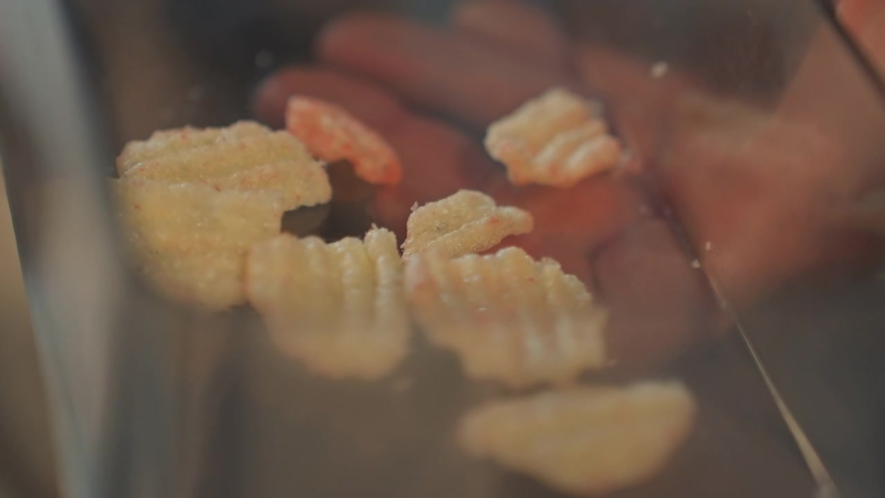 Person selects one piece from pile inside clear plastic. Details like visible crumbs and coating are seen. Blurred backdrop emphasizes foreground details of snack texture