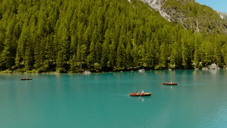 arial drone shot of boats rowing in the river, in the back there is a forest of pine trees, lago di braies, italy, dolomites