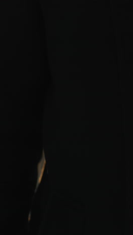 primer plano de un hombre de pie con expresión enfocada, con abrigo negro y camisa blanca, brillo suave de la luz del sol iluminando detrás de él, fondo borroso que muestra un edificio de vidrio urbano