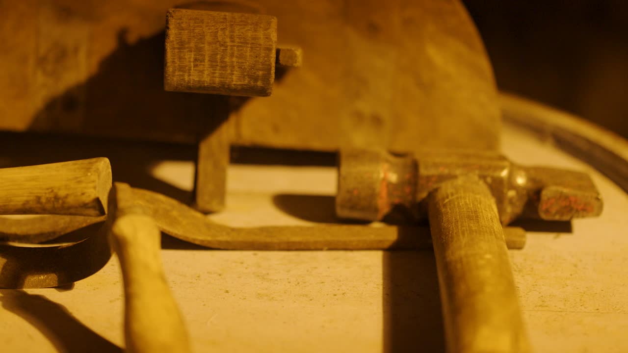 Close-up sequence of wooden mallet striking oak stave using vintage cooperage tools in a warm-lit distillery workshop, highlighting traditional barrel-making craftsmanship