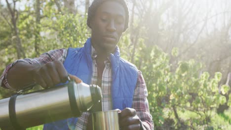 Afroamerikanischer-Mann-Im-Wald,-Der-Tee-Auf-Dem-Land-Gießt