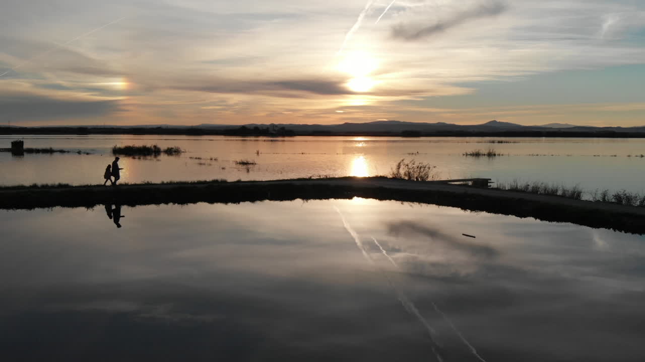 Aerial view fowards, Beautiful sunset over the rice field covered with water. Father and daughter standing on the path. Perfectly smooth surface of water in Albufera National park, Valencia Spain