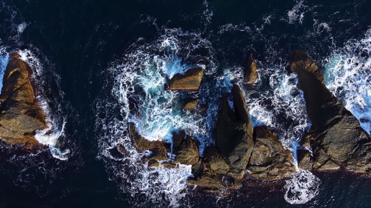 Waves crash over rocky formations, revealing the vibrant dance of nature beneath sunlight in a stunning coastal scene