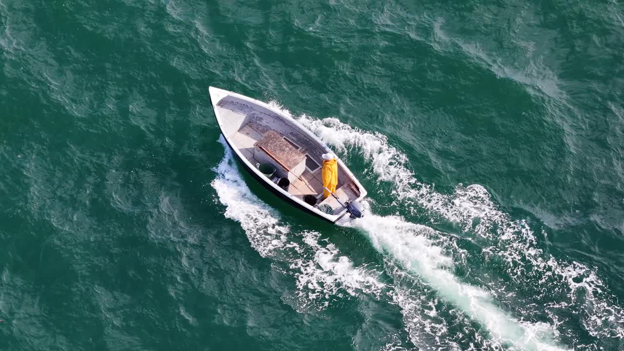 Aerial view of fishing boat with sailor moving through green sea, bright daylight, smooth tracking