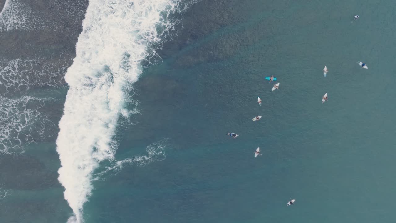 인도네시아 발리 루와투의 빙긴 해변에 있는 아름다운 푸른 물이 있는 저류 암초에서 파도를 기다리고 있는 서퍼들의  다운 드론