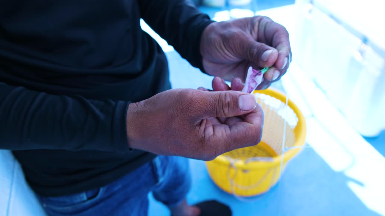 A person skillfully prepares fishing bait on a boat in Phuket, Thailand, under bright natural lighting