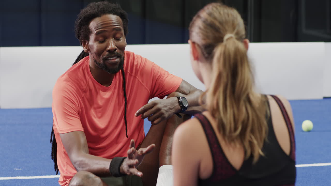 Coach discussing strategy with player on padel court, holding water bottle
