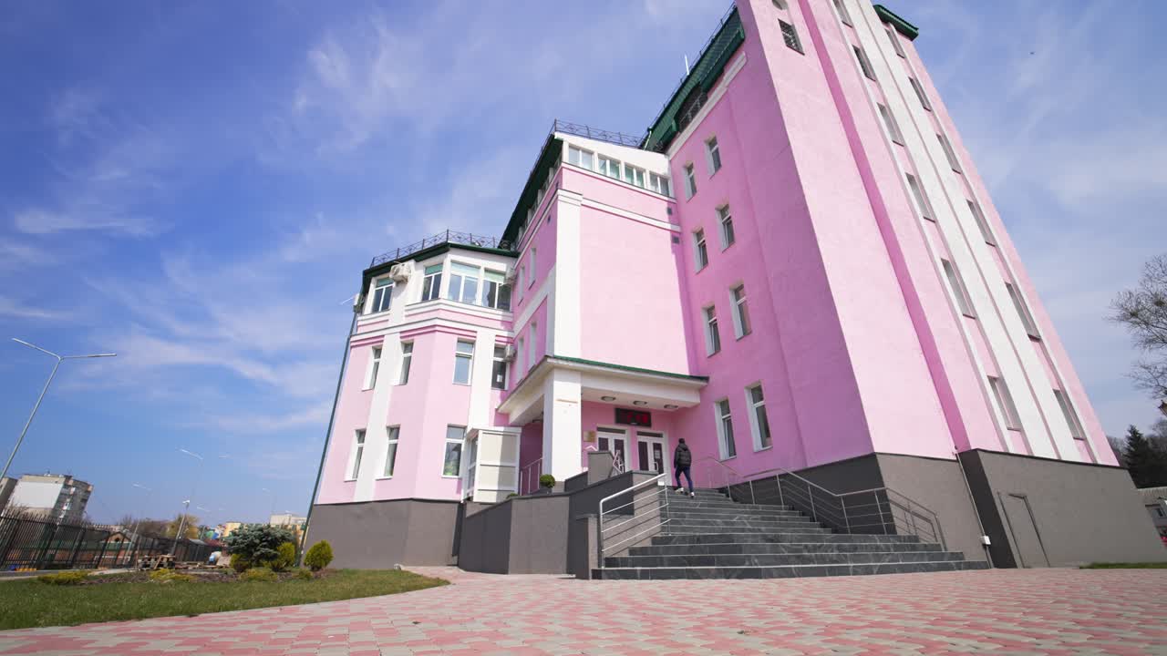 Nice pink building with grey stairs entrance. People coming up to the doors. Low angle view. Blue sky backdrop.