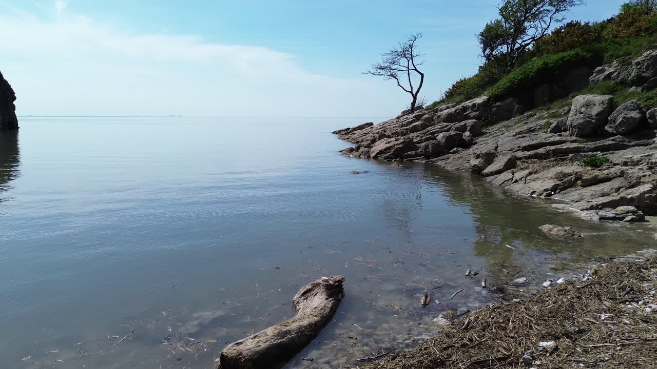 Rugged private rocky shoreline aerial view over mirrored waterfront reflection and calming tide
