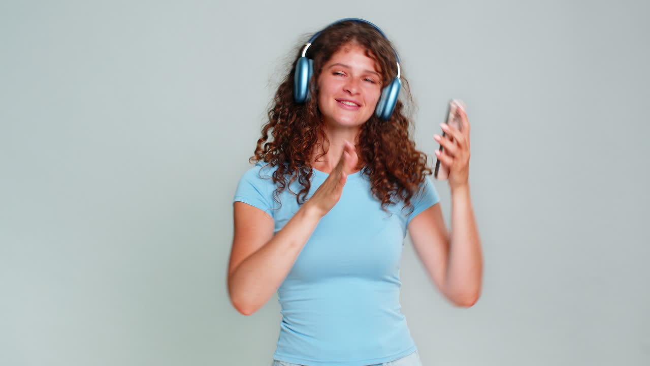 Woman dancing energetically spinning with smartphone wearing headphones carefree joyful movement