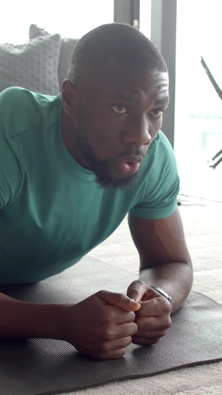 Man starting fitness routine, holding forearm plank and adjusting posture on mat beside smartphone