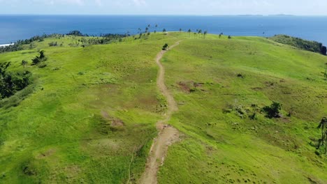 People-hiking-trail-on-green-rolling-hills-of-corregidor-island,-Siargao