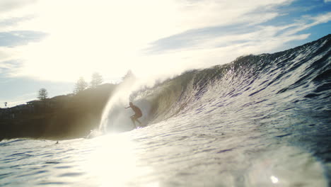 Golden light glints on barrel wave as surfer disappears inside powerful shorebreak in slowmo