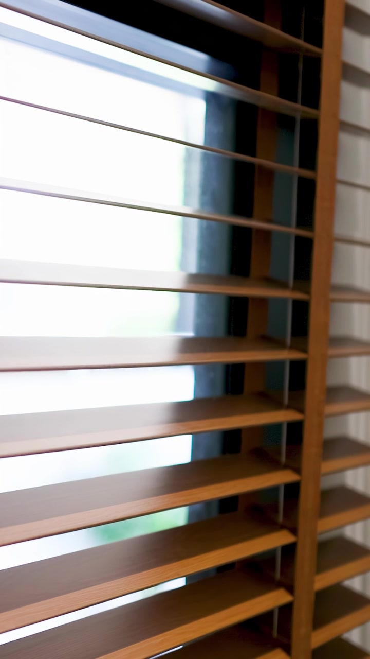 Person's Hand Closing Wooden Blinds to Block Out Light