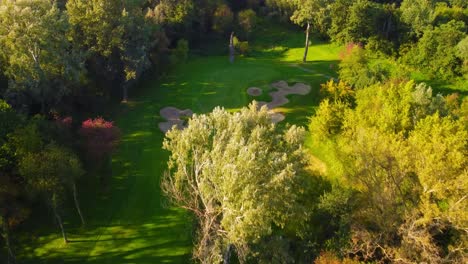 high angle establishing drone shot flying close trees above golf course, revealing sand bunkers and a golf hole during sunny, summer day in warsaw, poland