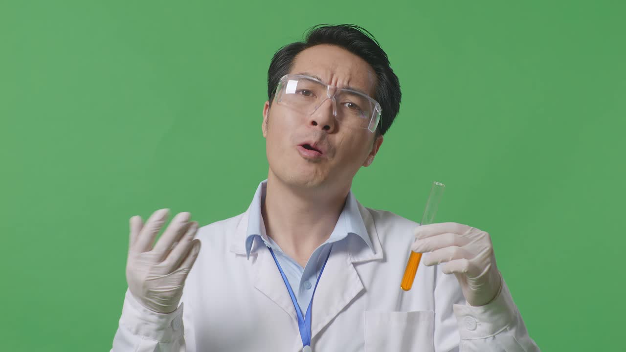연구실에서 녹색 화면 배경에서 의심스럽게 일하는 이유를 말하는 테스트 튜브에 오렌지 액체와 함께 궁금한 아시아 남자 과학자
