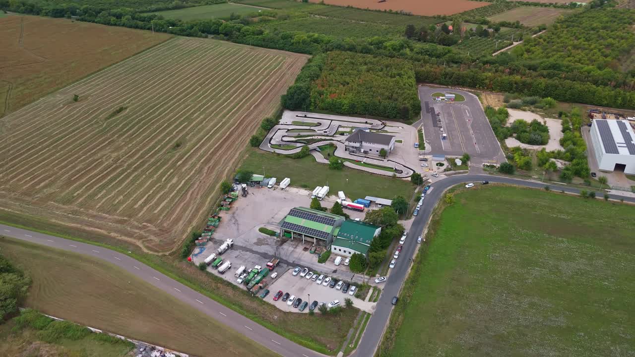 Aerial view of a go-kart track and a waste management facility on the edge of Százhalombatta, Hungary, with agricultural fields and greenery around