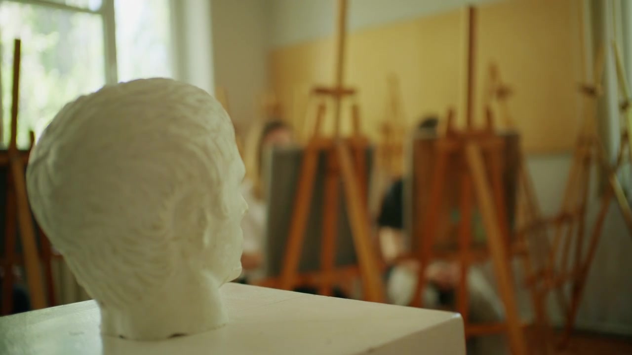 Weiße Skulpturenbüste in einem Kunstatelier, während Schüler im Hintergrund Zeichenübungen machen