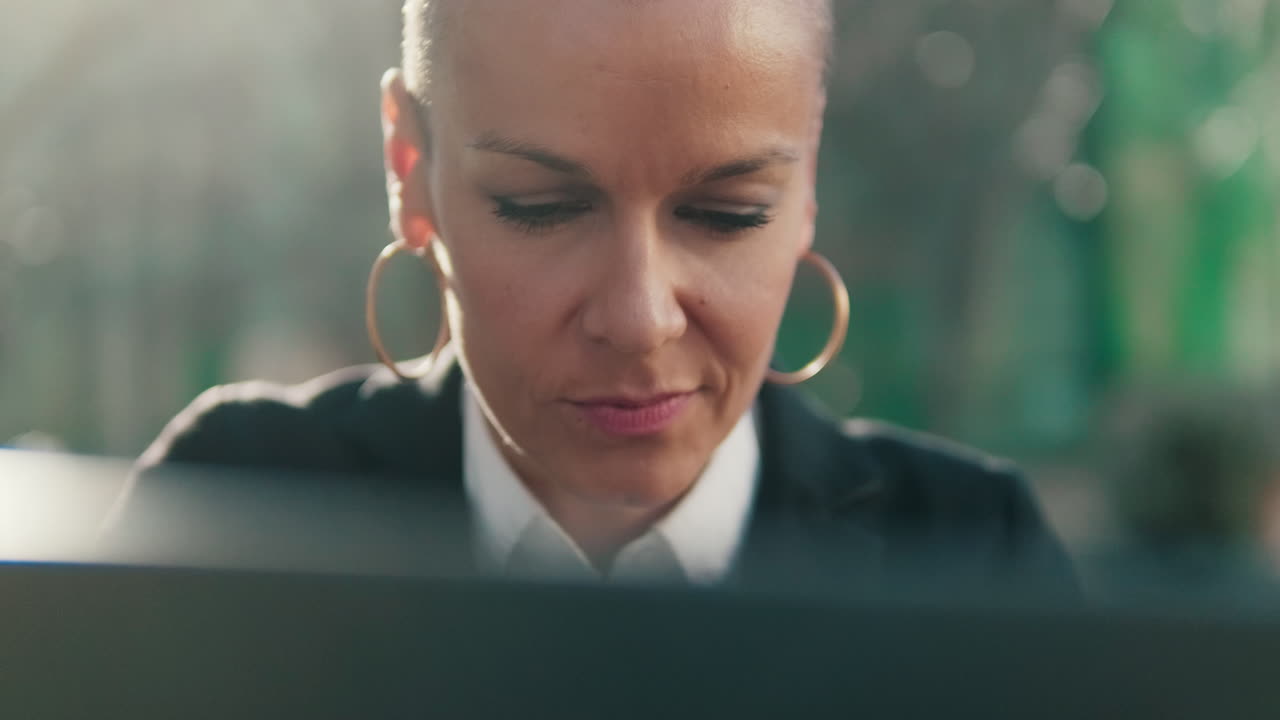 Fokuseret forretningskvinde med kort hår arbejder på bærbar computer udendørs
