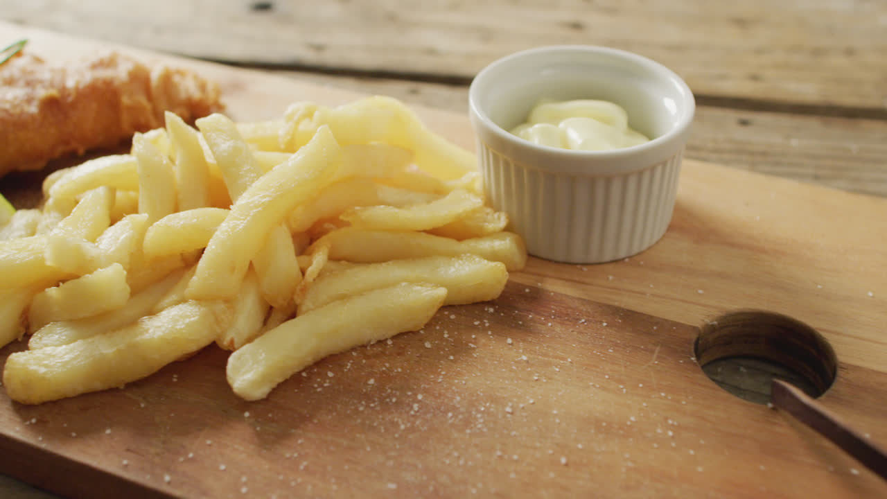 Video of fish and chips with lemon wedge and dip on wooden board, on rustic table