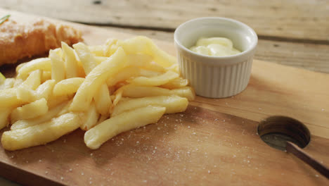 video of fish and chips with lemon wedge and dip on wooden board, on rustic table