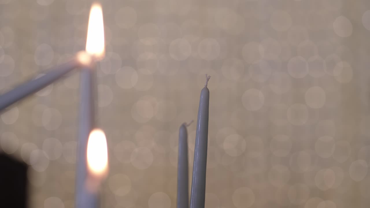 Close up of a hand lighting a taper candle using another with soft bokeh background light