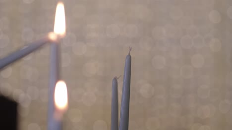 close up of a hand lighting a taper candle using another with soft bokeh background light