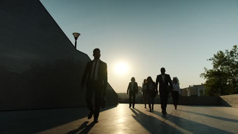 silhouettes of businesspeople walking outdoors near office building with sun rising in background