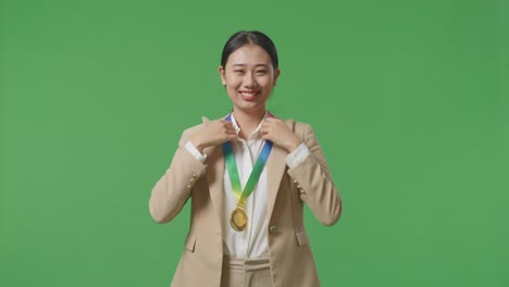 asian business woman in a suit wearing a gold medal and smiling to camera being proud winning as the first winner on green screen background in the studio