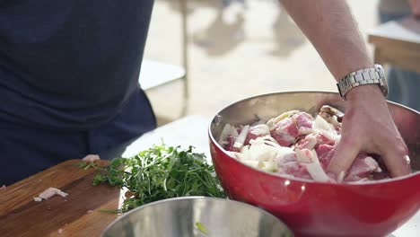 man is mixing meat pieces with spices and onion in metal bowl. the wooden surface outside. barbeque time. shot in 4k