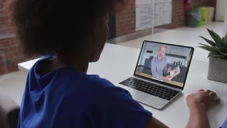 African-american-woman-talking-on-video-call-with-male-colleague-on-laptop-at-office