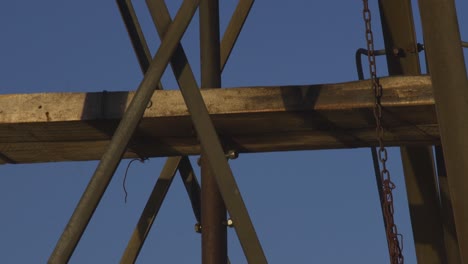 Old-windmill-structure-moving,-with-the-moon-in-a-blue-sky,-in-Patagonia,-Argentina