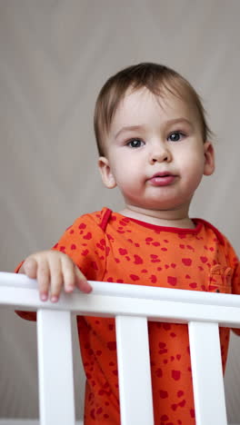 sweet calm caucasian baby standing calmly in the white bed. adorable kid looks up with interest and then laughs cheerfully. vertical video