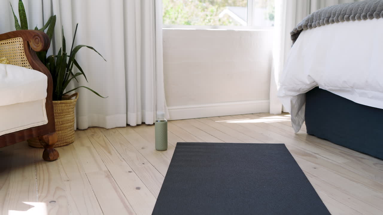Yoga mat on wooden floor in bright bedroom with cozy decor and natural light, copy space