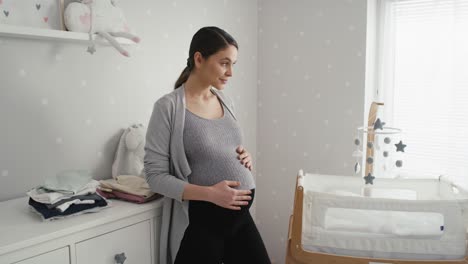 thoughtful caucasian woman in advanced pregnancy standing in the baby's room next to the crib.