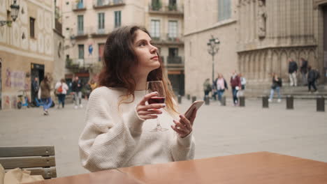 una joven sentada en un café bebiendo un vaso de vino tinto