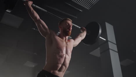 slow motion: brutal athlete lifts the bar above himself performing a jerk a spinning push. a man is engaged in weightlifting on a dark background portrait. concept strength power playing sports.