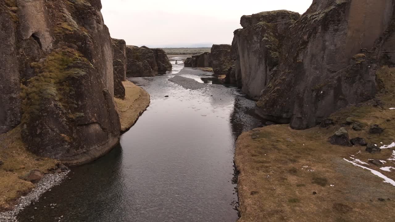 A calm river winds through the towering basalt cliffs of Fjaðrárgljúfur Canyon in southern Iceland, showcasing the raw, ancient beauty of this dramatic natural gorge.