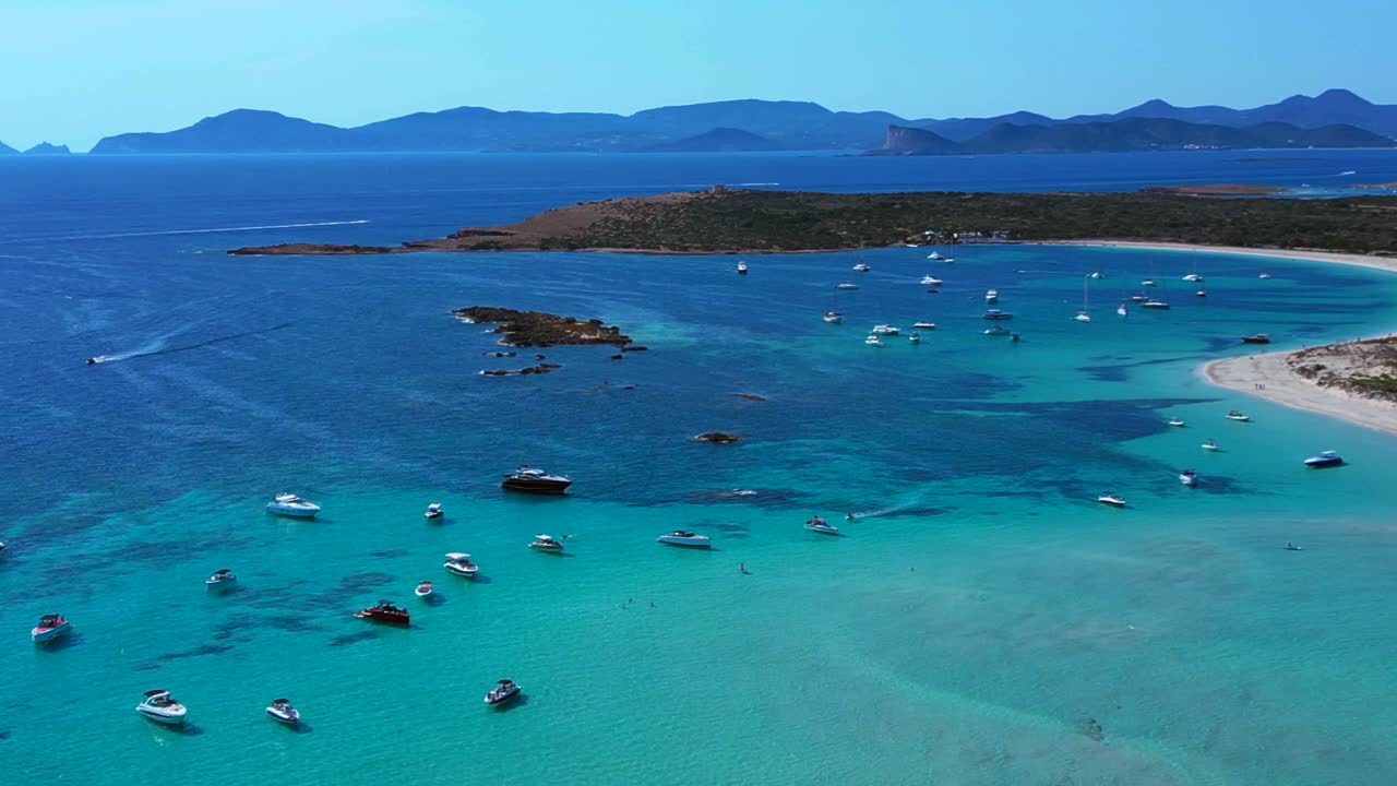 Espalmador island featuring white sand beaches, clear turquoise water, and anchored boats. Ibiza and the island of Es Vedra in the background. Magic aerial view flight