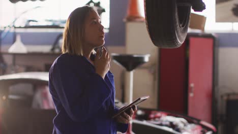 Animation-of-glowing-light-over-biracial-woman-working-in-car-workshop