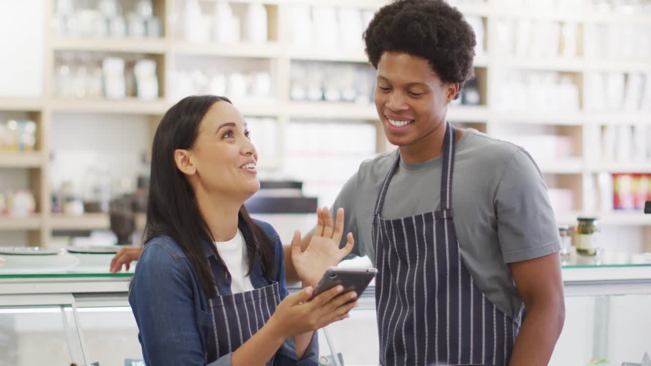 Animation of happy diverse female and male waiters using tablet at coffee shop and talking