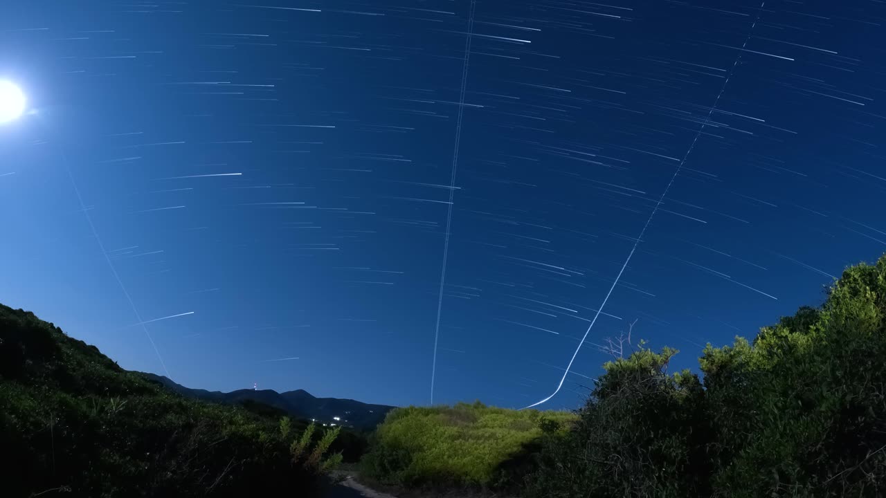 Time-lapse del cielo nocturno con estelas de estrellas y movimiento de satélites sobre un paisaje rural oscuro en Corfú (Grecia) que muestra la rotación terrestre y el concepto de astronomía