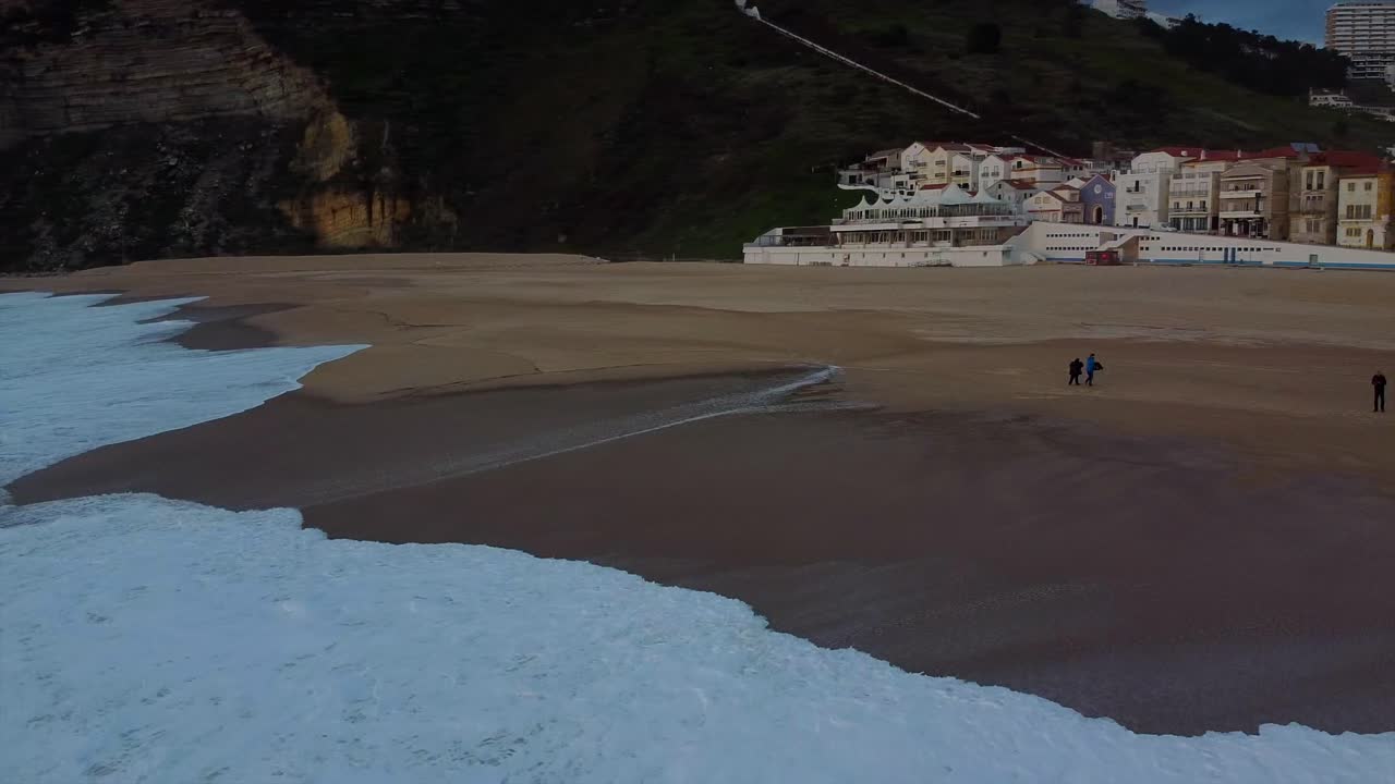 Carrellata aerea sulle onde con vista di un veicolo rosso dei bagnini sulla spiaggia di Nazaré