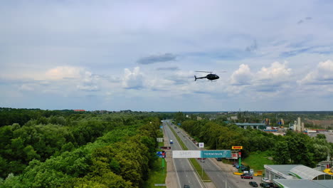 black helicopter is going to land near the gas station. construction site at backdrop. aerial view.