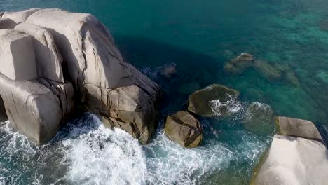 Vuelo-Aéreo-En-Cámara-Lenta-Sobre-Olas-Rompiendo-En-Rocas-Agua-Clara