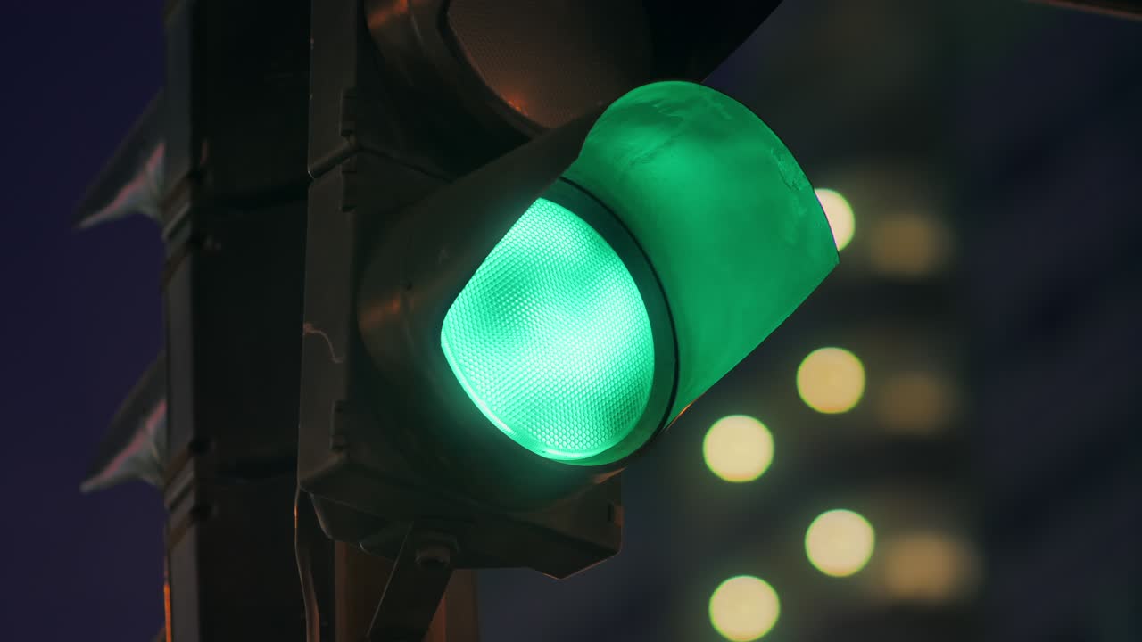 The traffic light against the background of the evening city lights up green, blinks and changes to orange